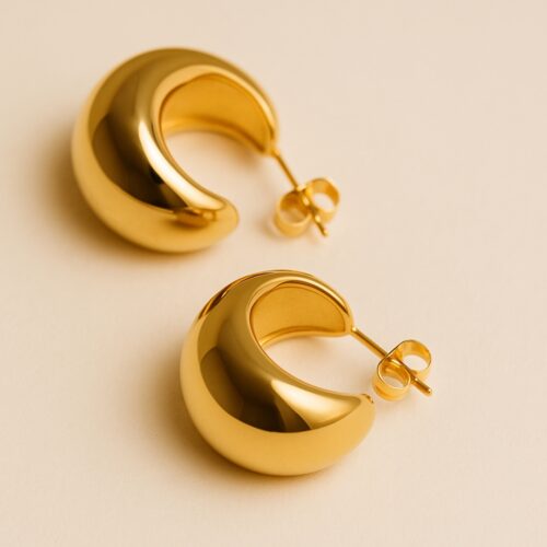 Aretes dorados abombados de acero inoxidable sobre fondo elegante, joyería moderna y atemporal para mujer