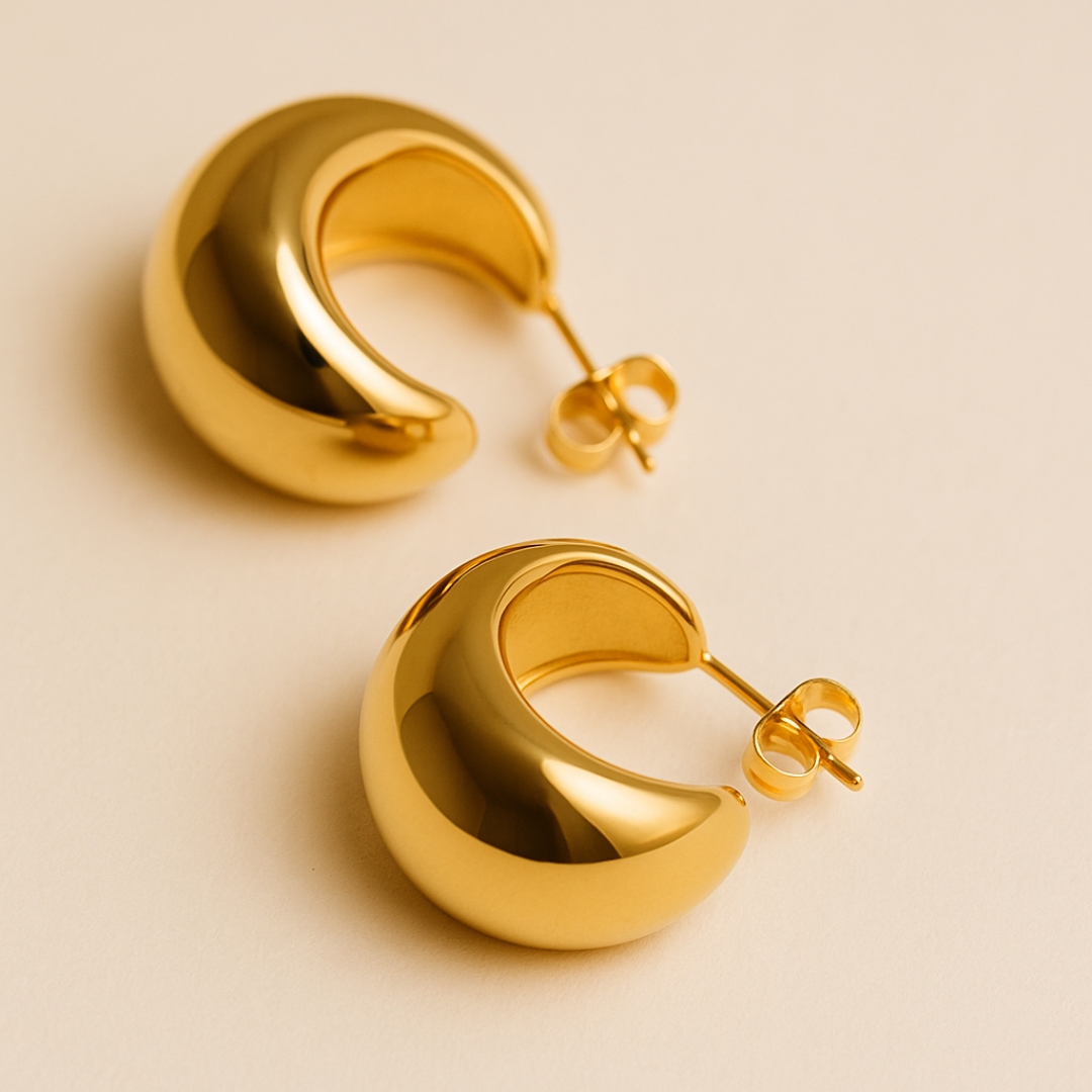 Aretes dorados abombados de acero inoxidable sobre fondo elegante, joyería moderna y atemporal para mujer