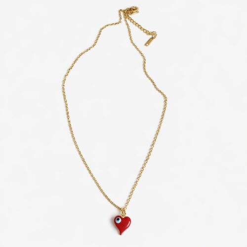 Gold necklace with red heart pendant and blue evil eye detail worn by a model in a white top.